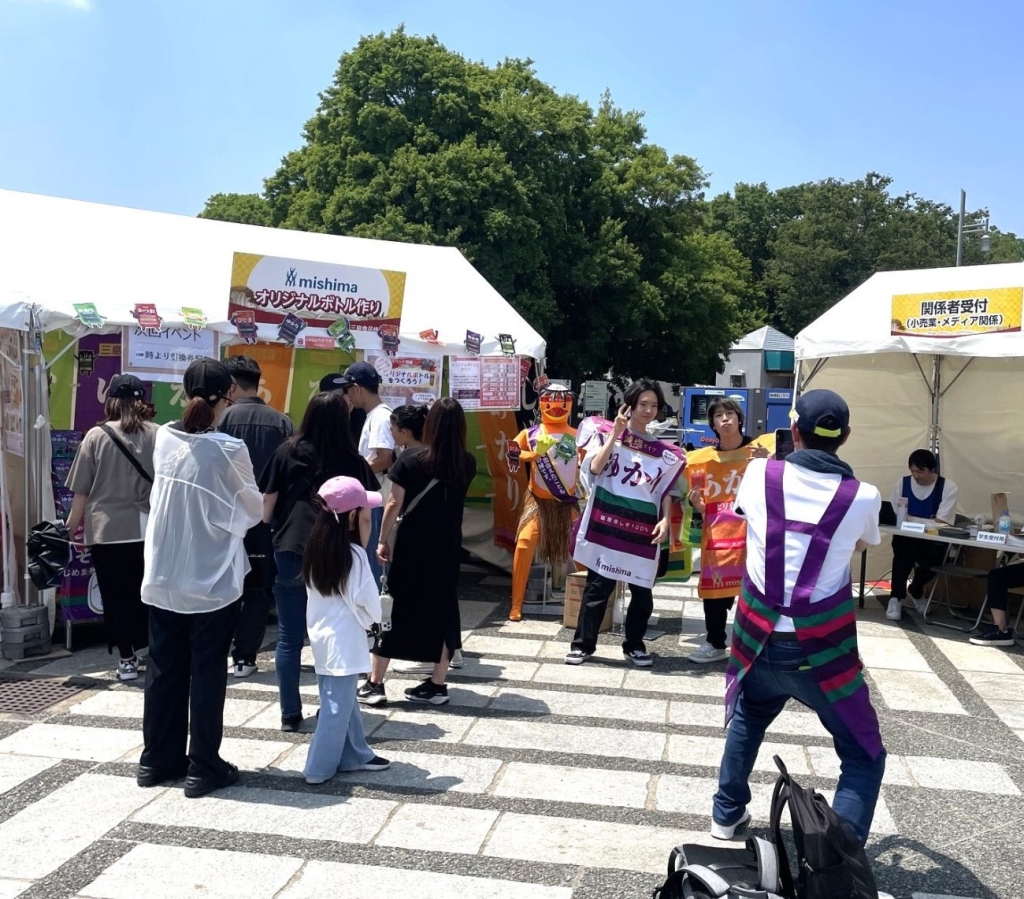 三島食品のブース、ふりかけを買う人やカッパを見る人、名前シリーズのポンチョを身にまとい記念撮影する人も