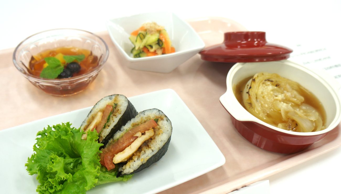 厚生労働大臣賞を受賞したメーキューの昼食メニュー（ジューシーチキンのおにぎりサンドやズッキーニのリボンサラダなど）